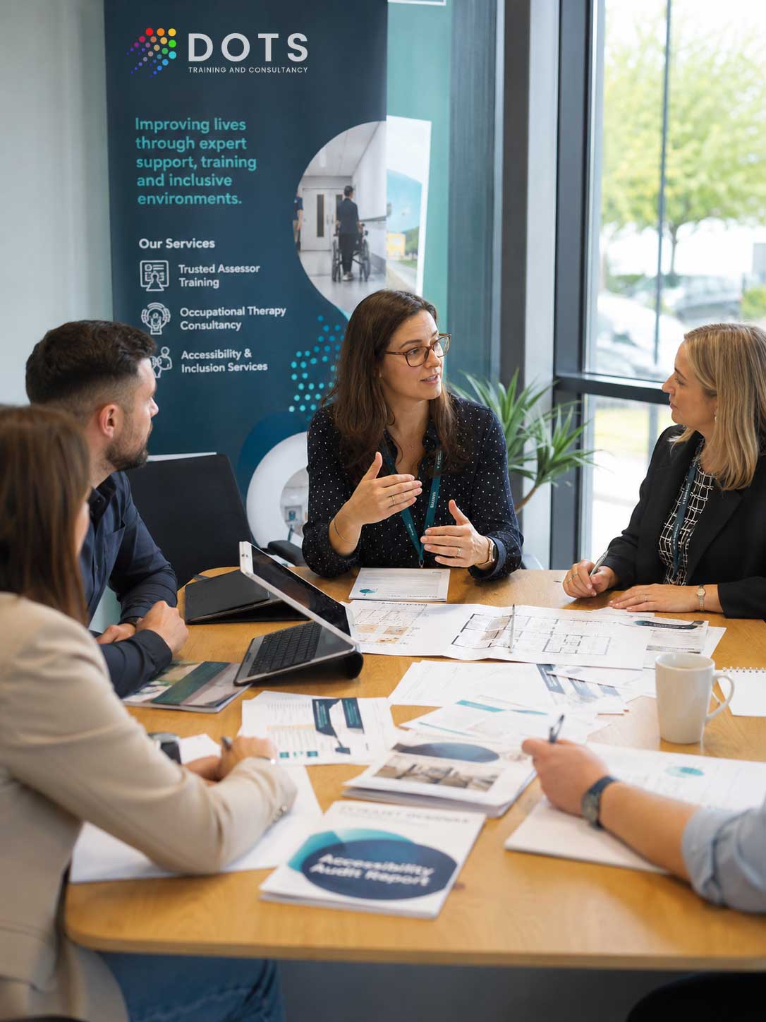 Experienced Occupational Therapist leading a collaborative consultancy meeting with housing, health and community service professionals reviewing assessment paperwork, accessibility plans and training materials.